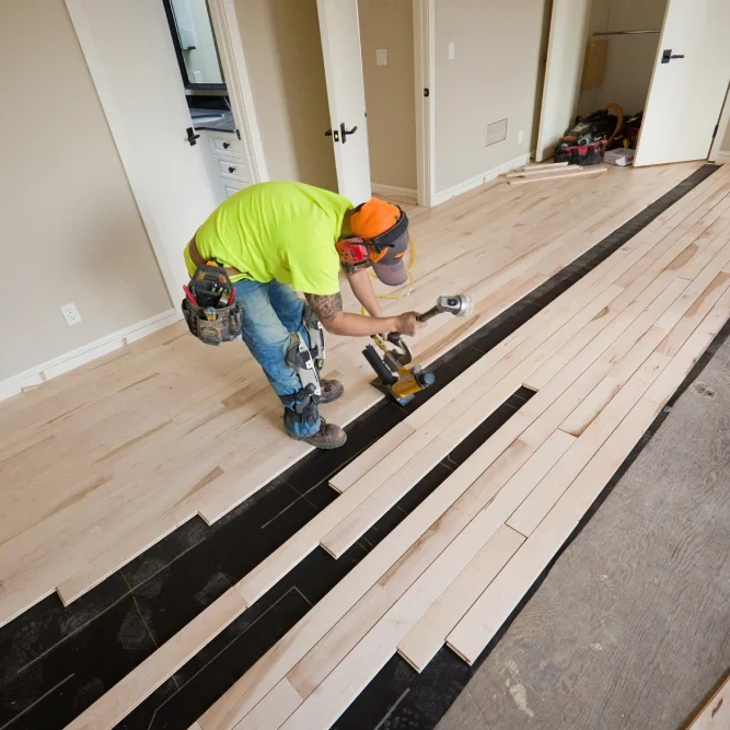 Worker installing hardwood floor in room.