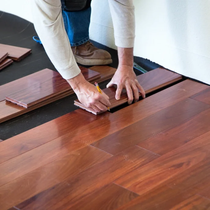 Person installing wooden flooring with tools.